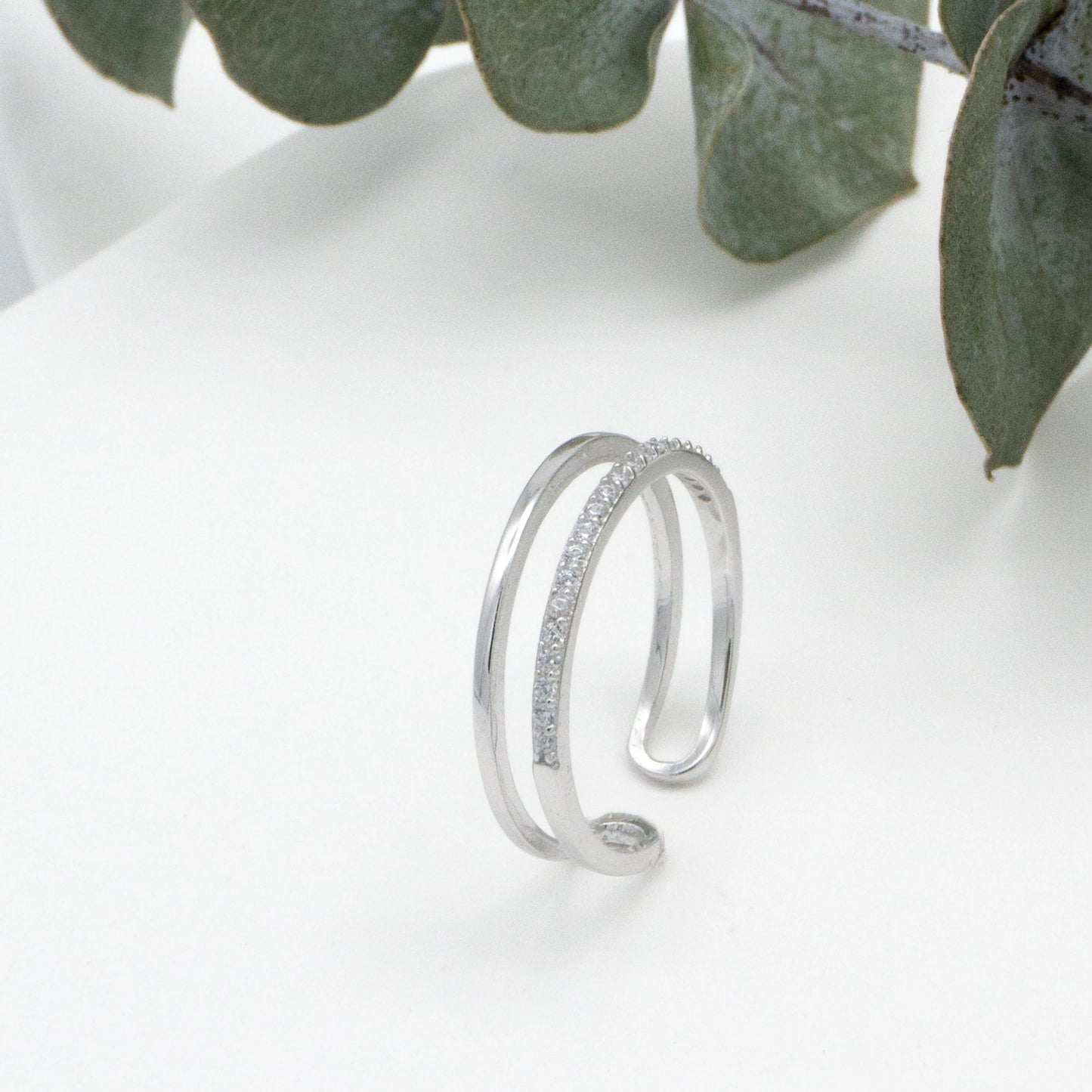 Anillo de plata con circonita en una mesa blanca junto a una planta.